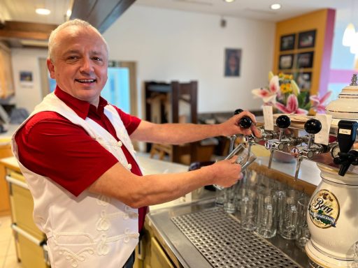 Ein lächelnder Mann bedient eine Bierzapfanlage in einem Gastronomiebetrieb.