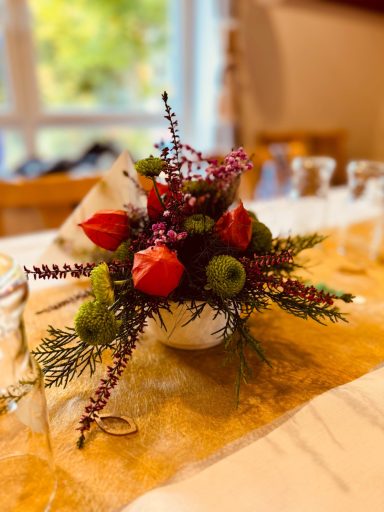 Bunte Blumenvase mit roten, grünen und lila Blüten auf einem gedeckten Tisch.