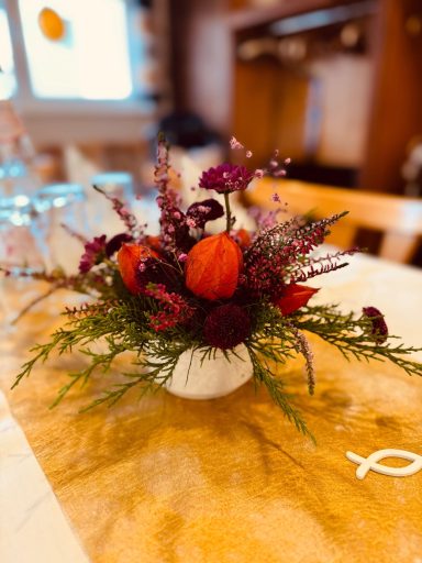 Blumenarrangement mit roten Tulpen und lila Akzenten in einem weißen Gefäß.