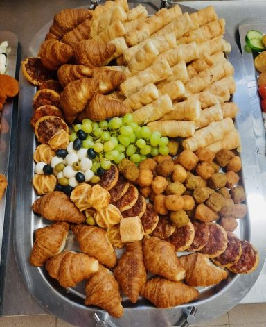 Vielfältige Auswahl an Gebäck, Obst und kleinen Snacks auf einem Tablett.