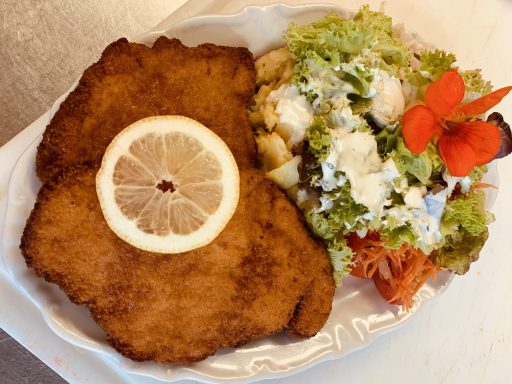 Panierte Schnitzel mit Zitronenscheibe und Beilage aus Salat und Dressing.