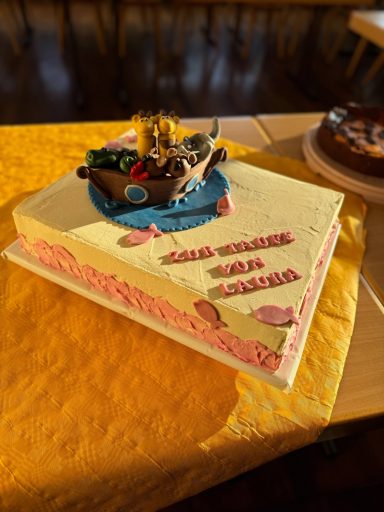 Torte mit maritimen Motiven und dekorativem Schiffsmodell auf gelbem Tisch.