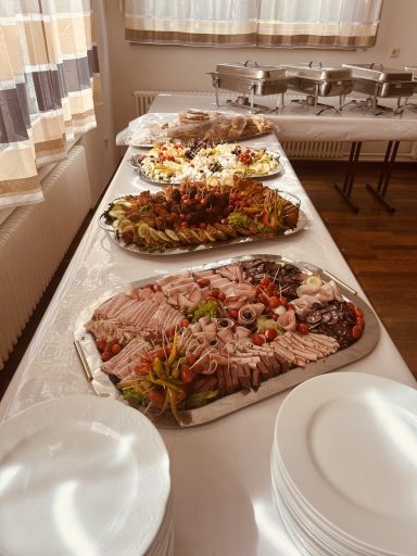 Buffet mit verschiedenen Platten, darunter Fleisch, Gemüse und Salate. Weißes Geschirr im Vordergrund.