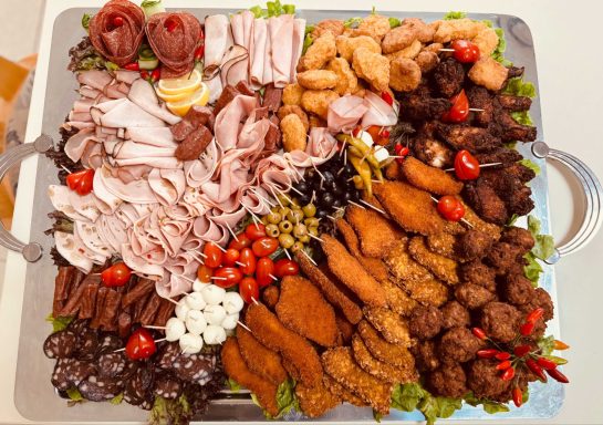 Eine Auswahl an Wurst, Fleisch, Käse, Oliven und Cherrytomaten auf einem Buffet-Teller.