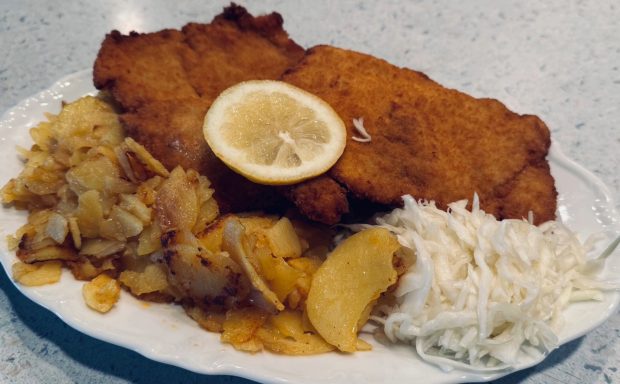 Schweineschnitzel mit Zitrone, Kartoffeln und Krautsalat auf einem weißen Teller.