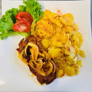 Rindersteak mit Zwiebeln, Bratkartoffeln, Salat und Tomatenscheiben.