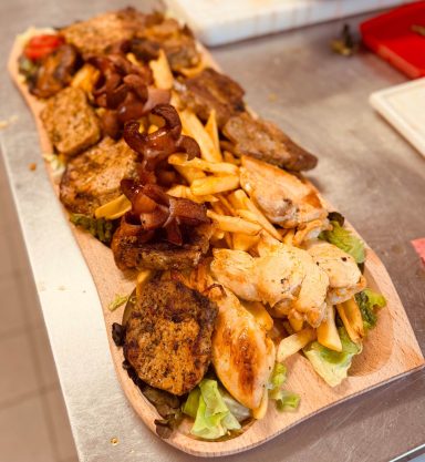 Ein Tisch voller gegrillter Fleischsorten, Pommes und frischem Salat.